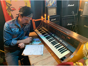 Julio César leyendo notas de una cancion junto al piano